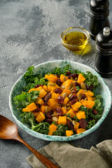 Fall salad with kale, roasted pumpkin, seeds and dried cranberries in bowl. Grey background. Mock up. Top view.