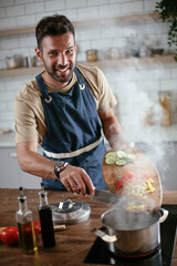 Wall Mural - Handsome man preparing pasta in the kitchen. Guy cooking a tasty meal..