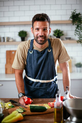 Young man preparing vegetable salad in the kitchen. Happy man making healthy meal.