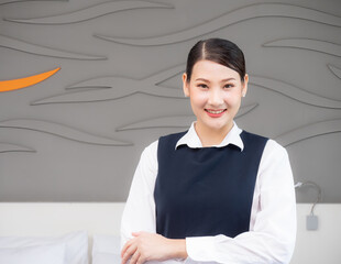 Portrait of attractive authentic Asian woman maid smiling in uniform standing with crossed hands and looking at the camera. Cleaning Service concept.