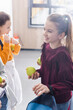 © LIGHTFIELD STUDIOS - Happy schoolgirl holding apple and backpack near friends on blurred background in school