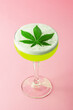 Alcoholic Cannabis Cocktail with THC CBD Infused Marijuana Liquor, Egg White Foam, and Pot Leaf Garnish on Pink Background