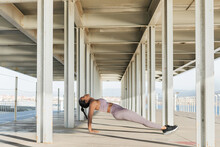 Side View Of Young Ethnic Female Athlete In Sports Clothes Training On Walkway Under Roof In Daylight