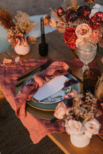 From Above Of Wooden Table Setting With Cutlery On Plates Served On Cloth Near Colorful Bouquets Of Flowers With Wineglasses During Wedding Celebration