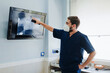 © Alberto Ortega/ADDICTIVE STOCK - Anonymous male vet in respiratory mask and uniform explaining anatomy of mammal animal while touching screen with X ray illustration in clinic