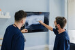 © Alberto Ortega/ADDICTIVE STOCK - Side view of unrecognizable male vets in masks interacting while looking at monitor with X ray illustration in hospital