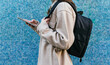 © David Munoz/ADDICTIVE STOCK - Side view of unrecognizable female student in casual wear with backpack standing against blue tiled wall