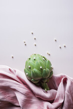 Top View Composition Of Fresh Healthy Artichoke With Small Beads Placed On Draped Fabric On White Background