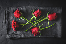 Top View Composition Of Bright Red Blooming Rose Buds Scattered On Black Surface With Cloth