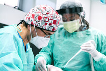 African American Nurse In Protective Uniform And Face Shield Assisting Professional Dentist In Face Mask During Procedure With Teeth Of Patient In Modern Stomatology Clinic During Coronavirus Pandemic