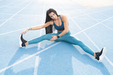 High Angle Of Flexible Female Athlete Sitting On Track And Stretching Legs While Doing Bends And Warming Up Before Workout At Stadium