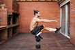 © Jordi Bataller/ADDICTIVE STOCK - Side view of focused male athlete with naked torso doing pistol squats on dumbbell and balancing on leg during workout on terrace