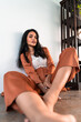 © Jordi Bataller/ADDICTIVE STOCK - Low angle of positive tranquil barefoot ethnic Indian brunette in stylish suit looking at camera while relaxing on floor in room