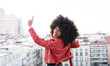 © Jose Carlos Cerdeno/ADDICTIVE STOCK - Back view of African American female with curly hair in stylish outfit standing on balcony and looking at city buildings