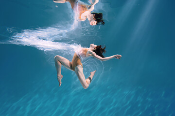 Wall Mural - Fashionable and athletic girl free diver alone in the depths of the ocean. Swimmer brunette diving deep in ocean on blue underwater background. Pollution, plastic and ecology concept