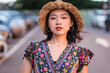 © Juan Alberto Ruiz/ADDICTIVE STOCK - Asian female in straw hat and with wicker handbag standing on parking lot and looking at camera