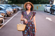 © Juan Alberto Ruiz/ADDICTIVE STOCK - Asian female in straw hat and with wicker handbag standing on parking lot and looking at camera