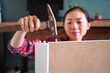 © Juan Alberto Ruiz/ADDICTIVE STOCK - Focused ethnic female using hammer for nailing wooden dowels while assembling new furniture in apartment