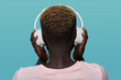 © Manuel Ruiz/ADDICTIVE STOCK - Back view of faceless African American female with short hair listening to music in headphones while standing against blue background