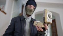 Close-up Of Robber Opening Decorative Box With Money Using Weapon. Blurred Armed Caucasian Masked Man Stealing Cash Dollars In Wealthy House Indoors. Break In And Robbery Concept.