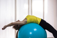 Side View Anonymous Fit Female In Activewear Stretching Back Muscles On Big Yoga Ball In Light Fitness Center