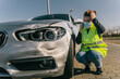 © Older Garcia/ADDICTIVE STOCK - Unhappy young female driver in yellow road safety vest and medical mask having phone conversation and checking damages on modern car parked on pavement after crash