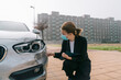 © Older Garcia/ADDICTIVE STOCK - Side view of unrecognizable female insurance agent in formal outfit and protective mask writing protocol near damaged car parked on street after accident