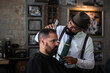 © Oscar Gimbal/ADDICTIVE STOCK - Stylish dandy serious ethnic male barber trimming hair of adult client with electric clipper in hairdressing salon