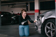© Older Garcia/ADDICTIVE STOCK - Upset young lady in casual clothes sitting on knees and touching damaged car headlights after accident in parking space