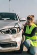 © Older Garcia/ADDICTIVE STOCK - Unhappy young female driver in yellow road safety vest having phone conversation and checking damages on modern car parked on pavement after crash