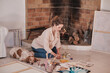 © Philippe Degroote/ADDICTIVE STOCK - Side view of female artist sitting on floor with sleeping Setter dog and creating artwork on paper with paints and brush in cozy house near fireplace