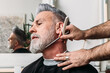 © Txema Gerardo/ADDICTIVE STOCK - Low angle of crop unrecognizable male barber shaving gray beard of middle aged stylish client in eyeglasses sitting near mirror in hairdressing salon