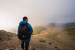 © Ruben Soto/ADDICTIVE STOCK - Back view of anonymous male trekker with rucksack standing on pathway against mount on misty day