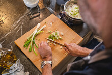 From Above Side View Of Crop Unrecognizable Male Chopping Fresh Green Onion On Cutting Board While Preparing Meal In Kitchen