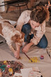 © Philippe Degroote/ADDICTIVE STOCK - Female artist cleaning paws of cute Setter dog from paint while sitting on floor with paper and paintbrush