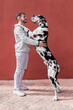 © Sergio Victor Vega/ADDICTIVE STOCK - Side view of happy young unshaven male in casual clothes and adorable obedient Harlequin Great Dane dog hugging each other against red background
