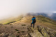 © Ruben Soto/ADDICTIVE STOCK - From above back view of anonymous male traveler with backpack taking photo of mount on camera on foggy day