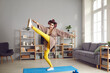 © Studio Romantic - Happy woman doing leg swings at home. Funny young housewife in hair curlers enjoying stretching exercise during sports workout in the living-room. Fitness and shaping your body humorous concept