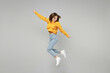 Full length of young excited overjoyed happy fun positive expressive woman 20s wearing knitted yellow sweater jumping high with outstretched hands isolated on grey color background studio portrait..