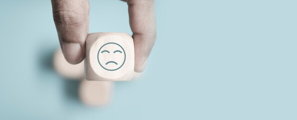 Wall Mural - World mental health day concept or feedback rating and positive customer review, Businessman hand holding sad face, wood cube with sadness face icon on pastel blue background