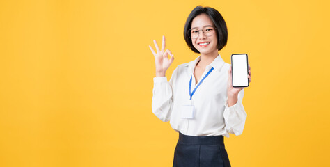 Cheerful beautiful Asian woman holding smartphone on light yellow background.