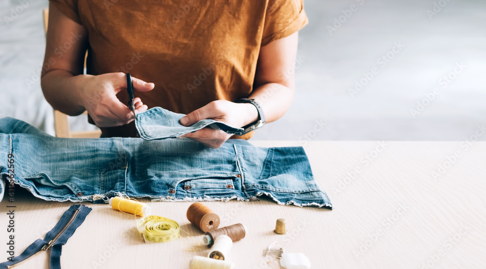 Woman repairs sews reuses fabric from old denim clothes economical reuse - obrazy, fototapety, plakaty 