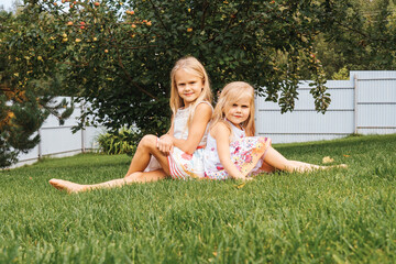 Happy childhood: Little girls sitting on grass. Close up portrait of little beautiful girls.