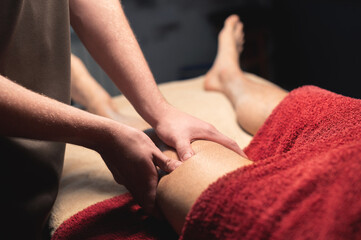 Wall Mural - Close-up Masseur man doing thigh massage of the leg to a man athlete client in a dark room of a massage spa