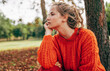 © iuricazac - Caucasian young woman resting in the park. Female wearing an orange knitted sweater has pensive expression posing on the nature background.