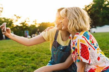 Sticker - Image of laughing two women in sunglasses taking selfie on smartphone