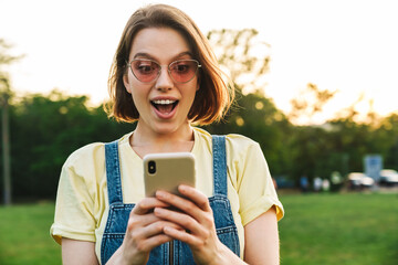 Sticker - Image of excited nice woman expressing surprise and using cellphone