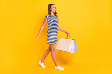 Poster - Full length body size view of pretty cheerful girl walking carrying new things bags outlet isolated on bright yellow color background