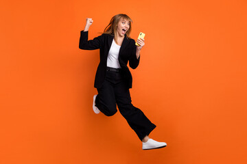 Sticker - Full size photo of happy crazy smiling good mood woman jumping win lottery in phone isolated on orange color background