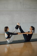 © BASILICOSTUDIO STOCK - A Pair sporty yoga women doing Balance exercise on gray stylish industrial background. Caucasian brunette girls training Pilates pose together in a fitness studio, health club.